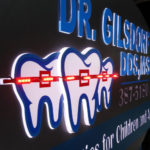 Closeup of neon sign for Dr. Gilsdorf DDS, MS featuring teeth with neon braces logo